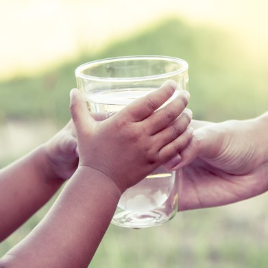 Woman hand giving glass of fresh water to child in the park,vintage color filter